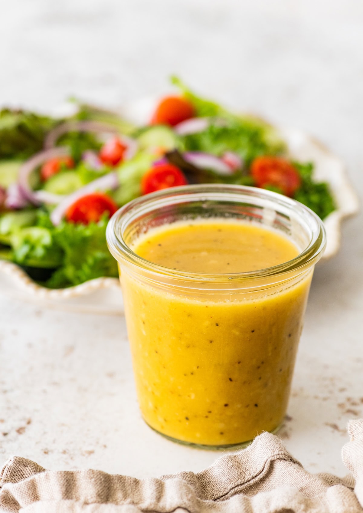 A glass jar with a golden/yellow apple cider vinegar dressing and a fresh salad in the background.