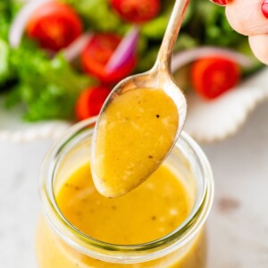 A woman holds a spoonful of dressing over a glass jar with apple cider vinegar dressing.