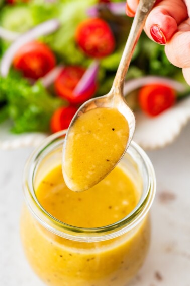 A woman holds a spoonful of dressing over a glass jar with apple cider vinegar dressing.
