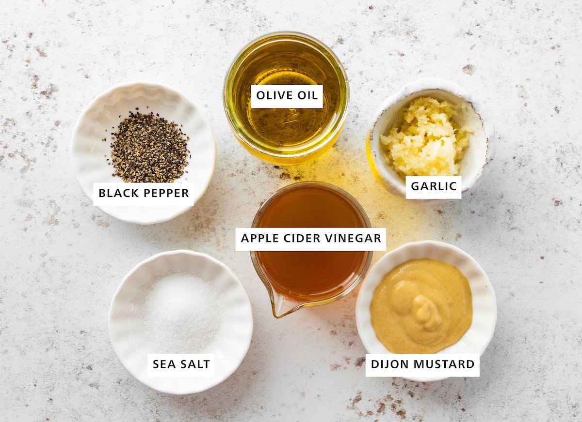 Ingredients measured out for apple cider vinegar dressing: apple cider vinegar, olive oil, garlic, dijon mustard, sea salt, and black pepper.
