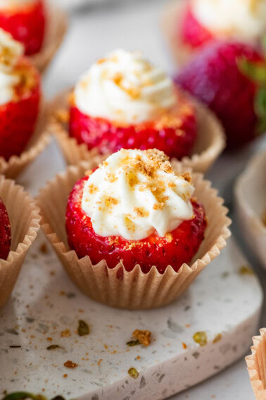 A cheesecake stuffed strawberry in a small cupcake liner topped with crushed graham crackers.