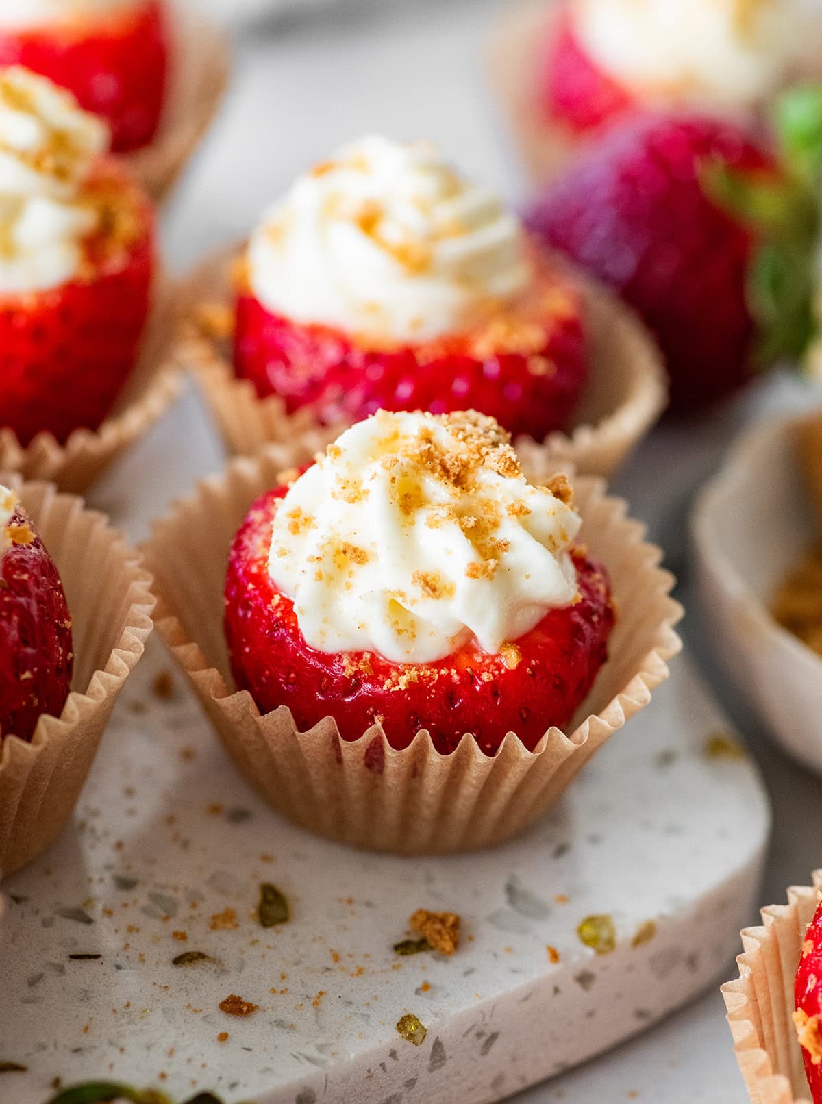 A cheesecake stuffed strawberry in a small cupcake liner topped with crushed graham crackers.