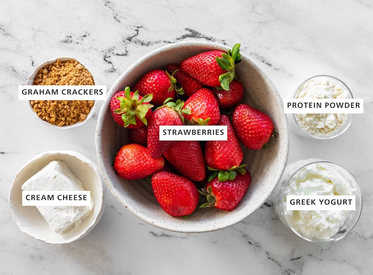 Ingredients measured out for cheesecake-stuffed strawberries: graham crackers, strawberries, protein powder, greek yogurt, and cream cheese.