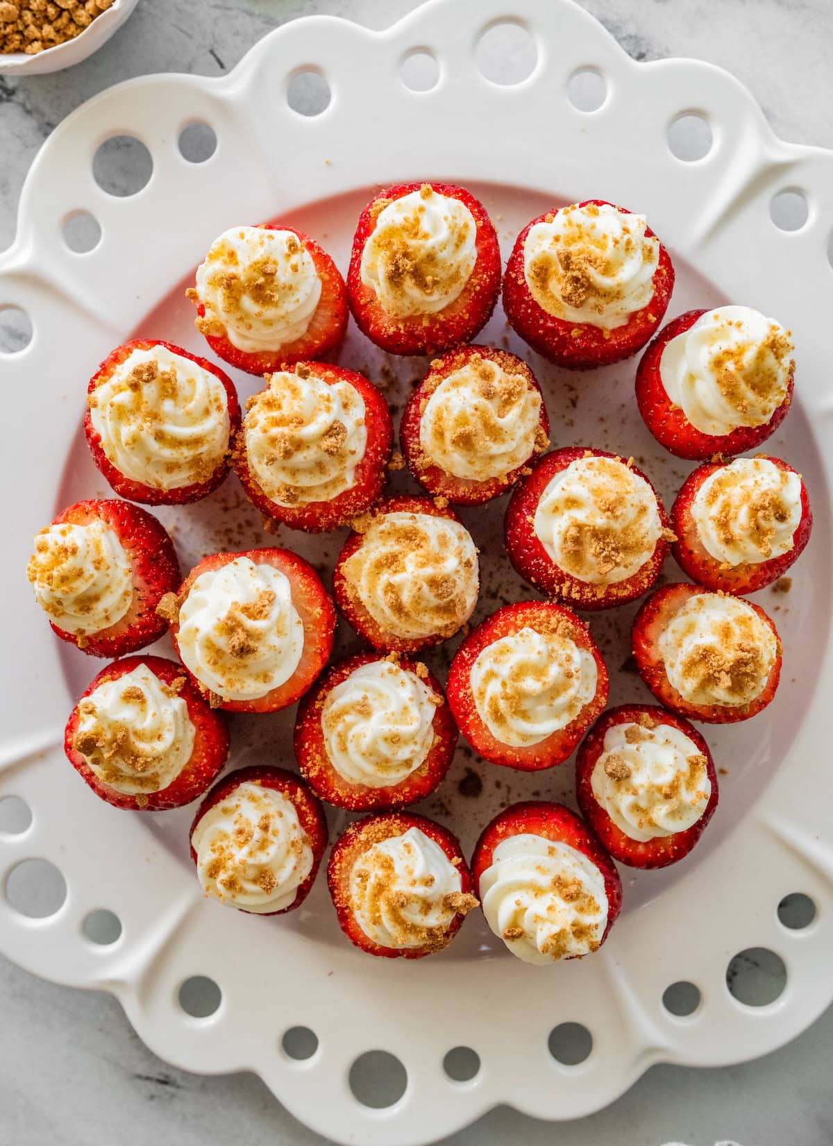 Cheesecake-stuffed strawberries on a large white plate, topped with crushed graham crackers.