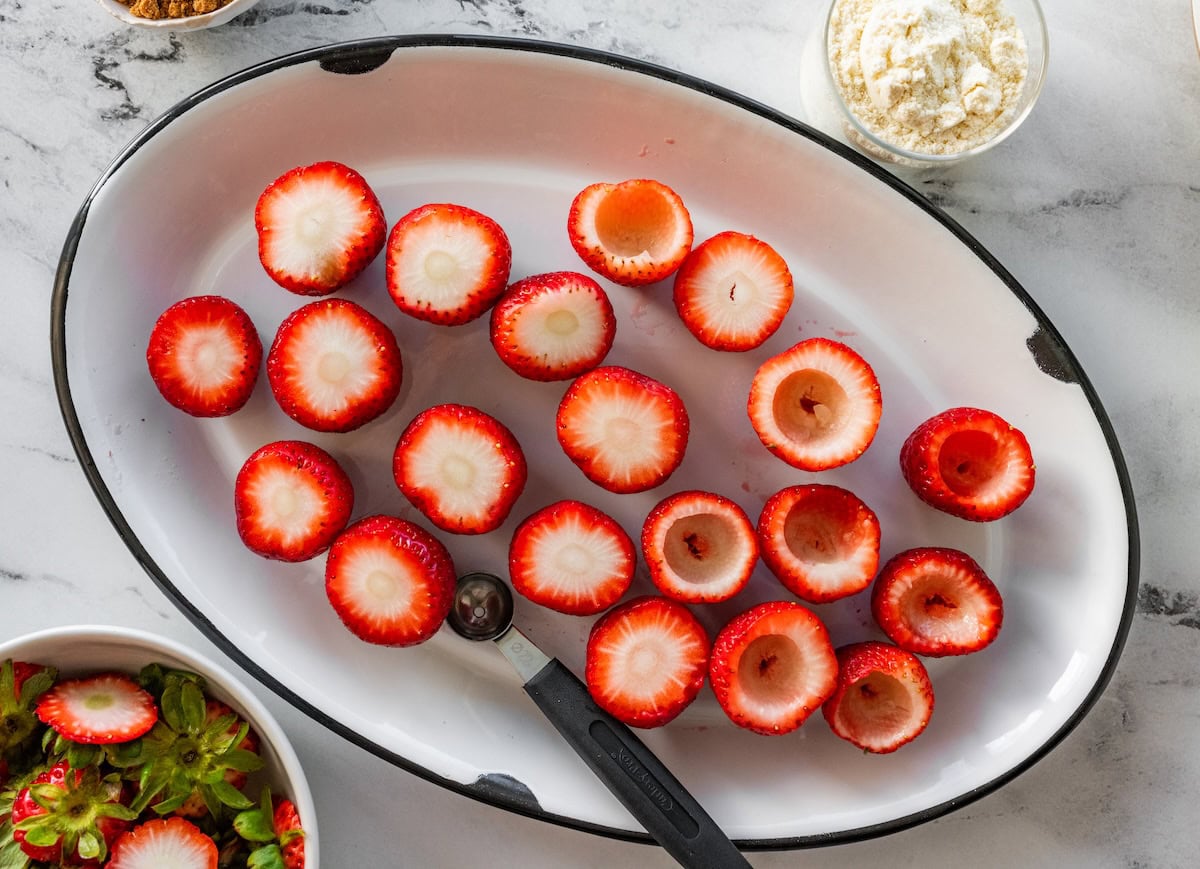 Strawberries in a large serving bowl with a small spoon nearby to hollow them out.