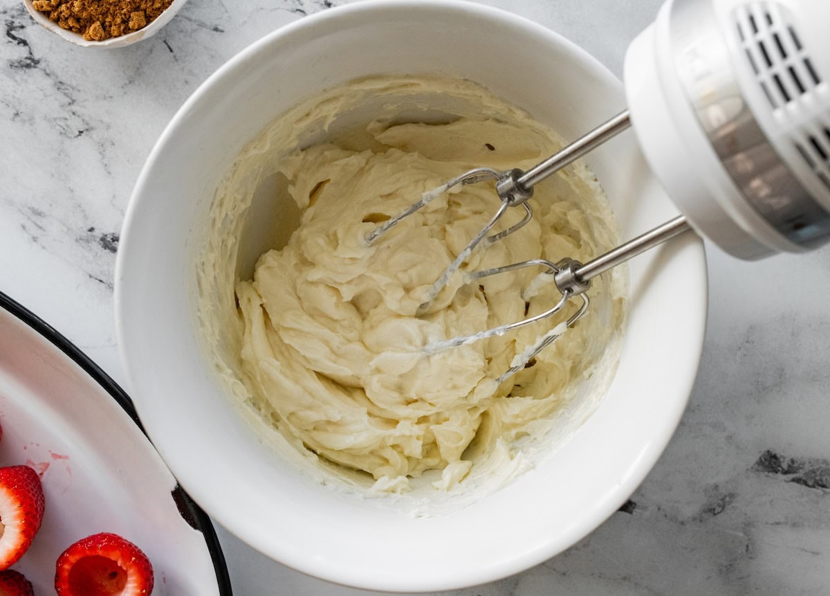 A hand mixer in a large mixing bowl with a cream cheese and yogurt mixture.