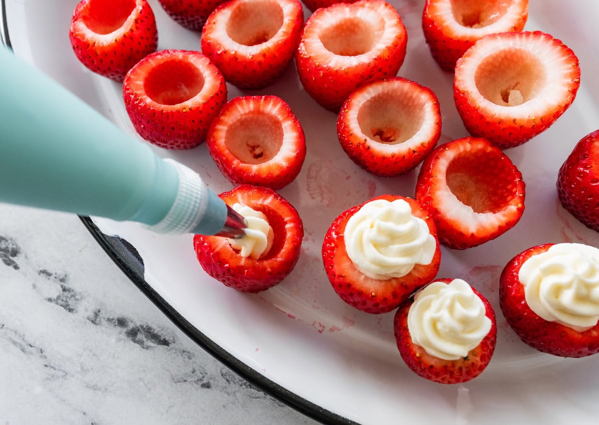 A piping bag is used to pipe a cream cheese and yogurt mixture into hollowed out strawberries.