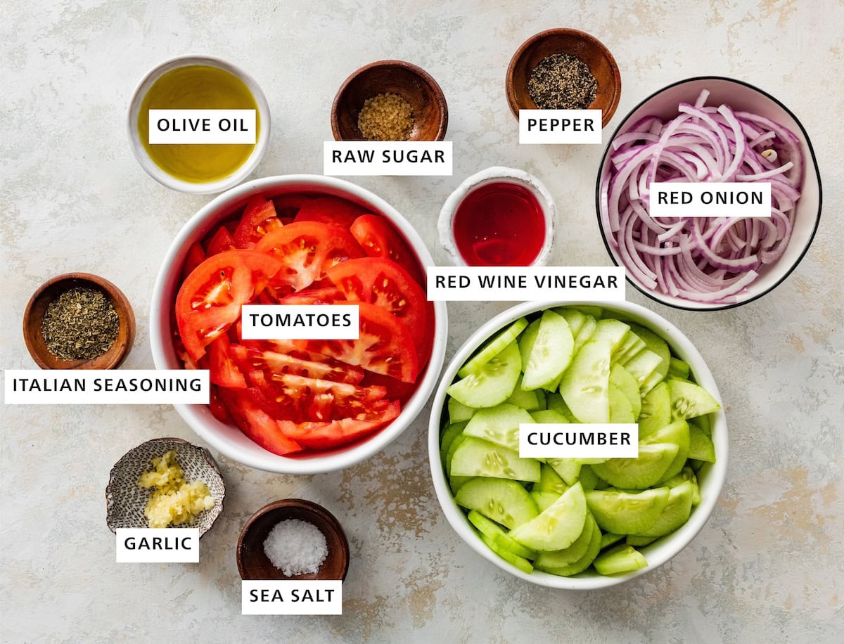 Ingredients measured out to make Cucumber Tomato Salad: red onion, cucumber, pepper, red wine vinegar, raw sugar, tomatoes, sea salt, olive oil, Italian seasoning and garlic.