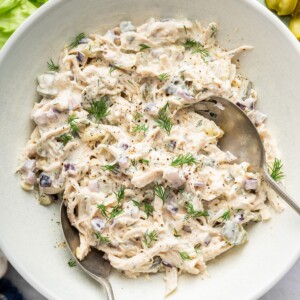 Dill pickle chicken salad in a large serving bowl with two serving spoons and topped with fresh dill.