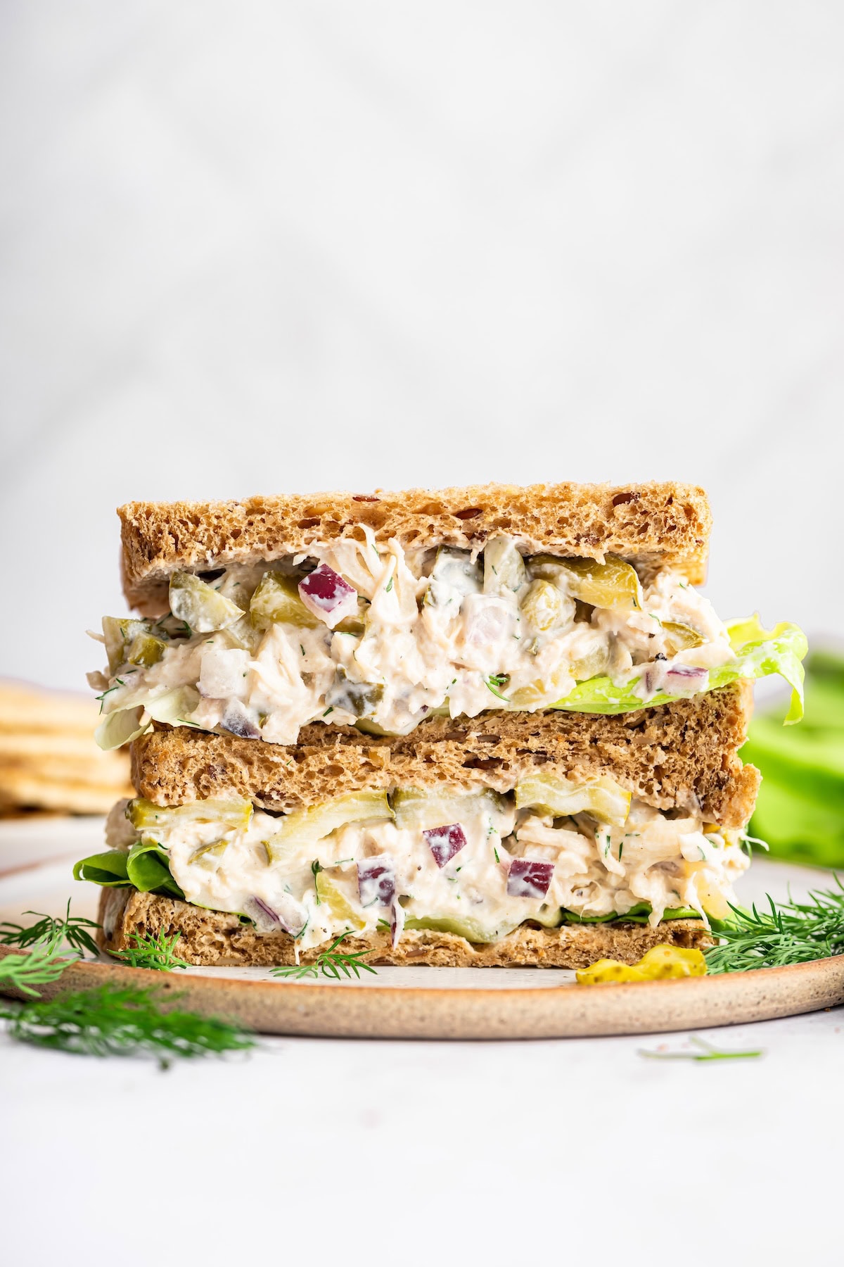 Two sandwich slices stacked on one another on a plate with a serving of dill pickle chicken salad in the sandwich.