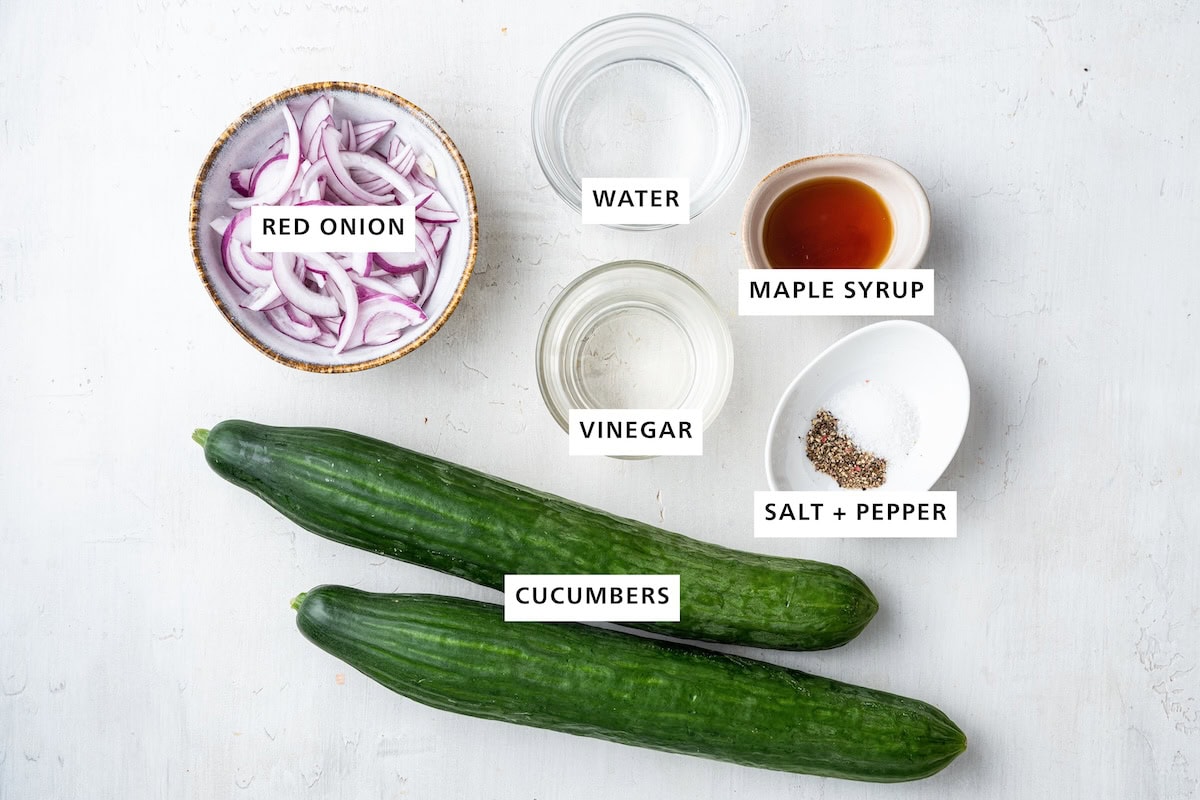 Ingredients measured out for a cucumber salad: Cucumbers, red onion, water, vinegar, salt, pepper, and maple syrup.