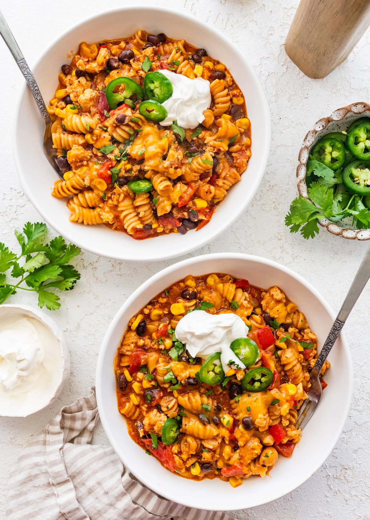 Two bowls of enchilada pasta topped with sour cream, jalapeno slices and fresh cilantro.