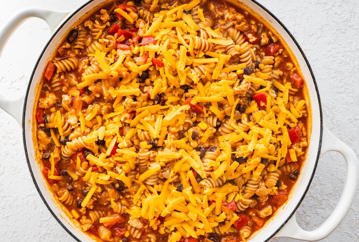 Shredded cheese added to the enchilada pasta in a Dutch oven.