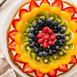 Sugar cookie fruit pizza topped with strawberries, mandarin oranges, kiwi, blueberries, blackberries and raspberries arranged in a colorful pattern.