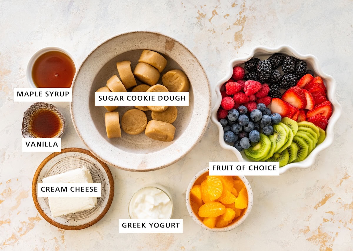 Fruit pizza ingredients: fresh fruit, greek yogurt, cream cheese, sugar cookie dough, vanilla and maple syrup.