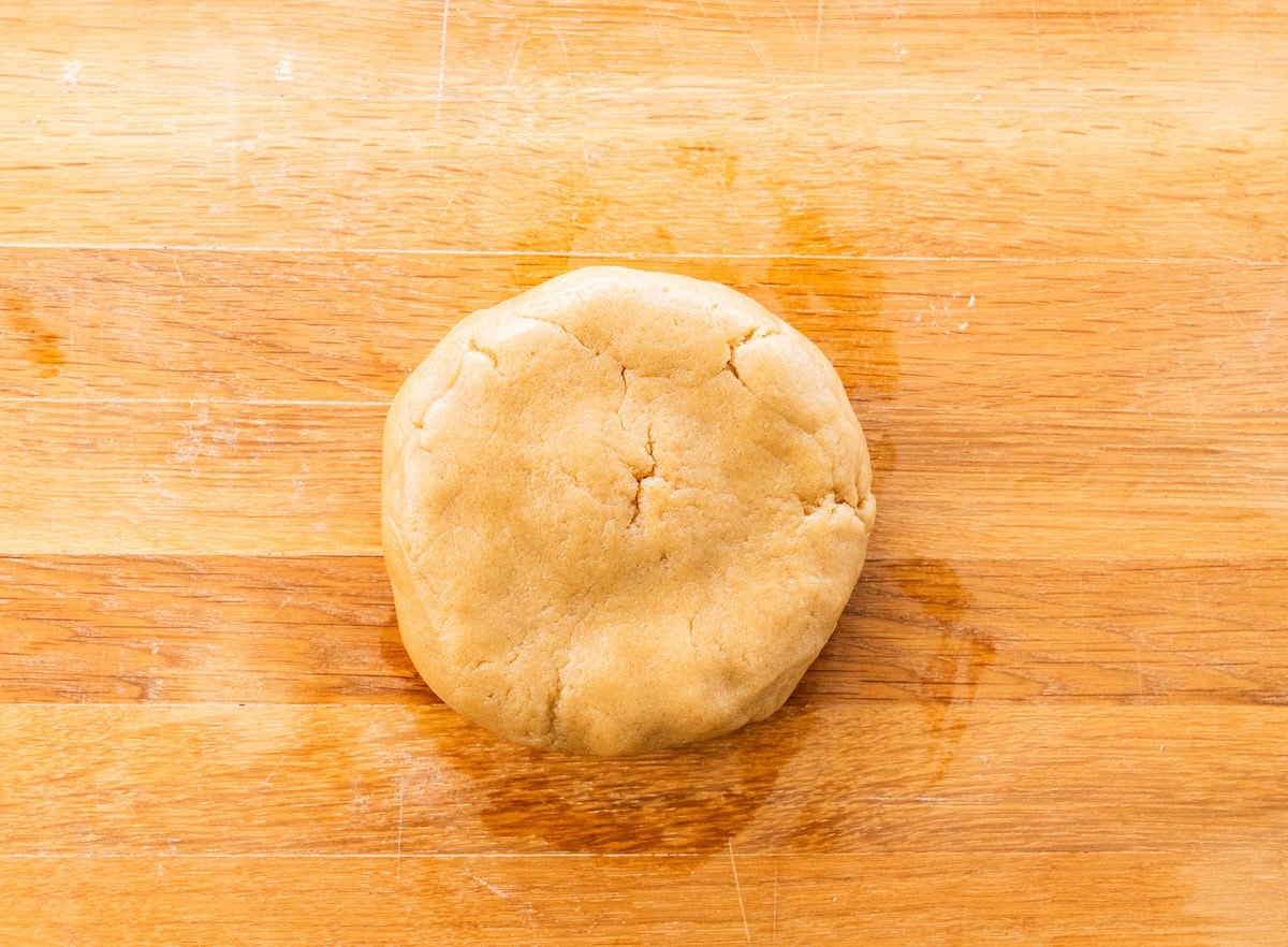 Ball of sugar cookie dough on a wooden surface before pressing into crust.