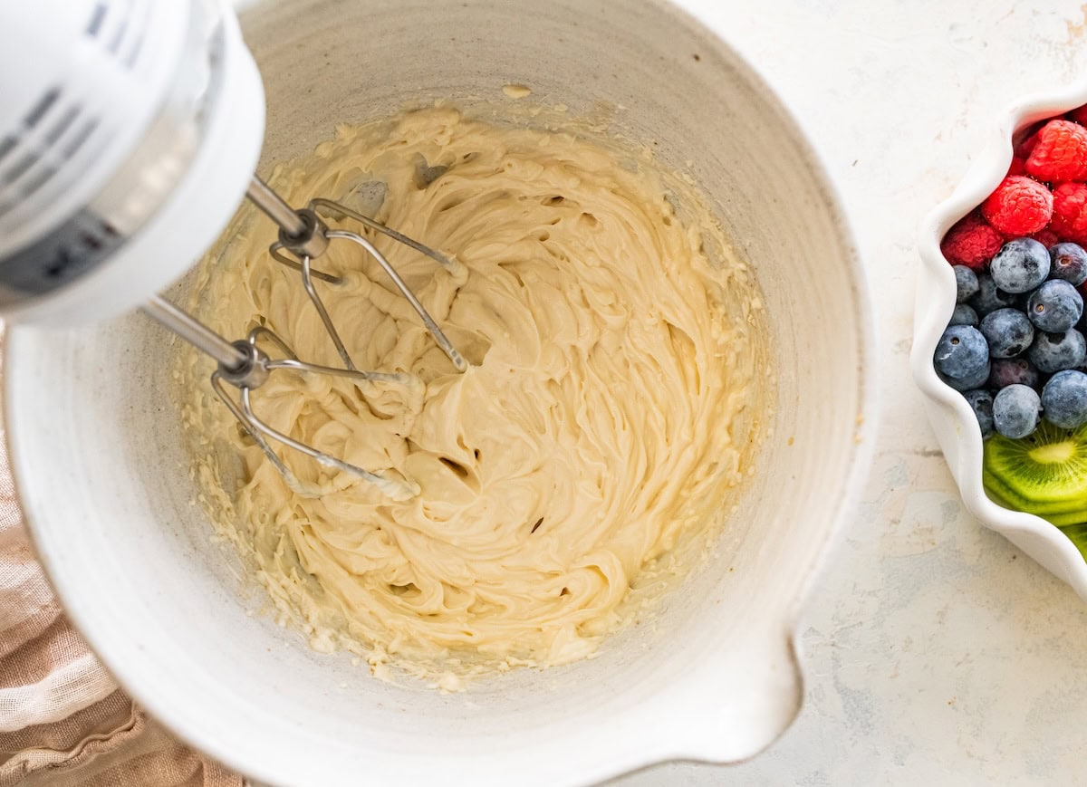 Mixing bowl with whipped cream cheese frosting being whisked until smooth.