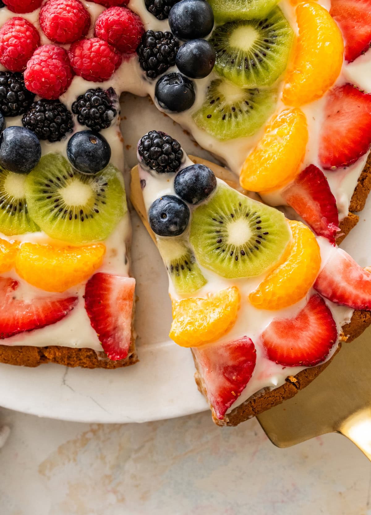 Sliced fruit pizza showing strawberries, kiwi and mandarin oranges, blueberries and blackberries on a sugar cookie crust