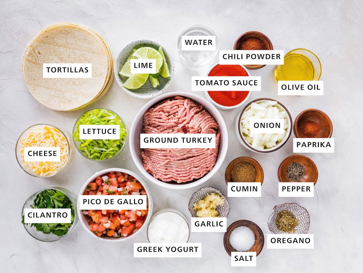 Ingredients measured out to make Ground Turkey Tacos: olive oil, paprika, pepper, oregano, chili powder, onion, cumin, salt, tomato sauce, garlic, water, ground turkey, Greek yogurt, lime, lettuce, pico de gallo, tortillas, cheese and cilantro.