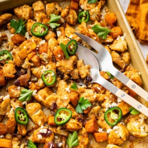 Hot honey glazed chicken on a baking sheet with roasted cauliflower, sweet potatoes, jalapeño slices, feta, and cilantro.