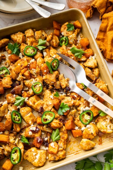 Hot honey glazed chicken on a baking sheet with roasted cauliflower, sweet potatoes, jalapeño slices, feta, and cilantro.