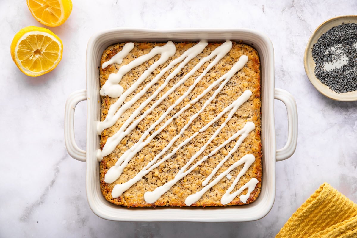 Baked lemon poppy seed oatmeal in a white dish topped with creamy yogurt glaze drizzle.