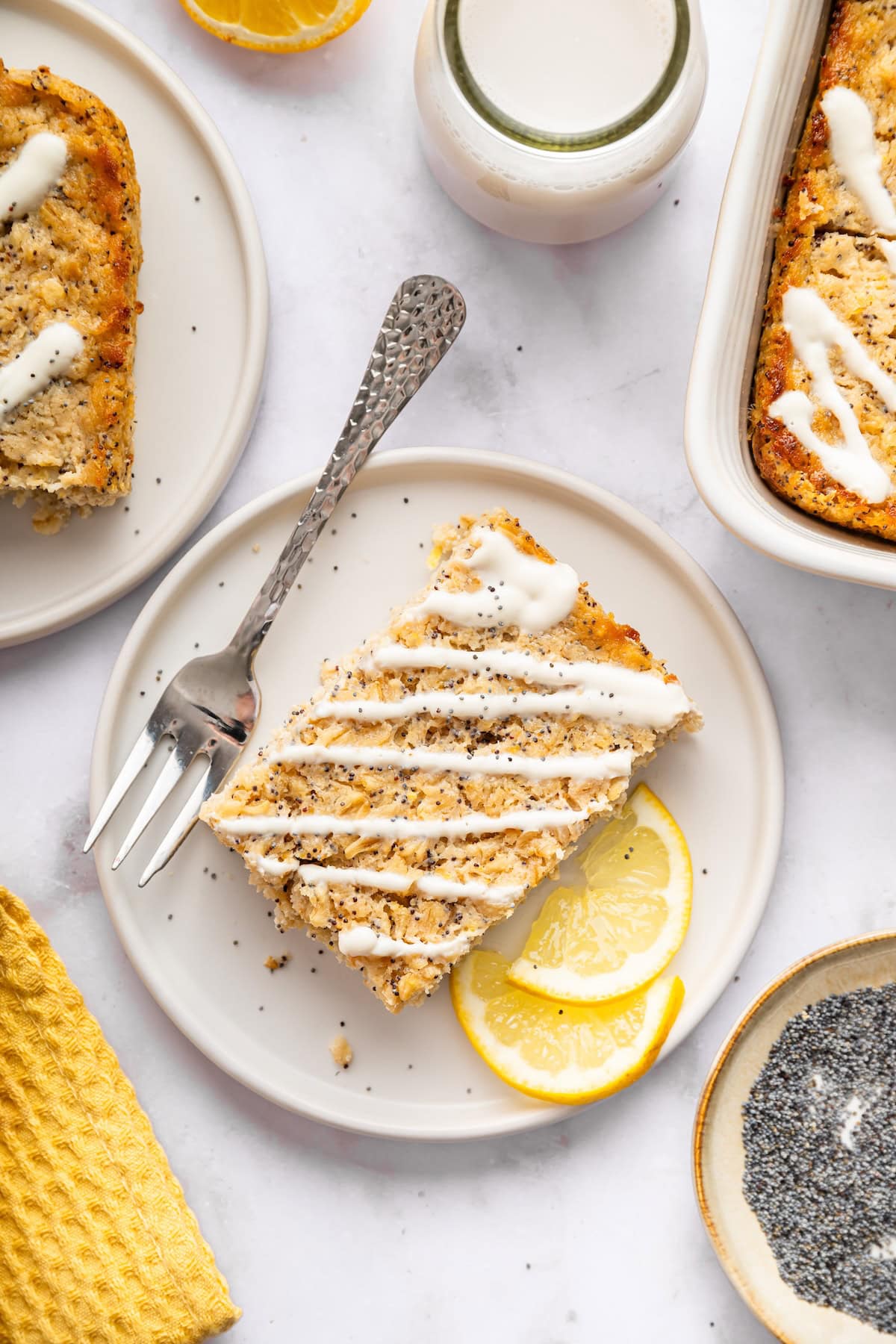 Two slices of lemon poppy seed baked oatmeal on white plates topped with a drizzle of yogurt lemon glaze.
