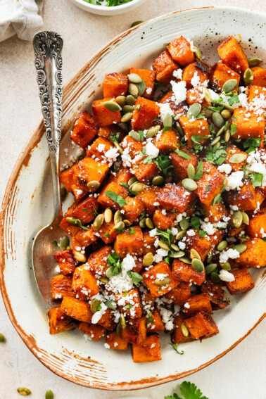 Rroasted Mexican sweet potatoes served on a platter garnished with cotija cheese, pepitas, cilantro and hot honey.