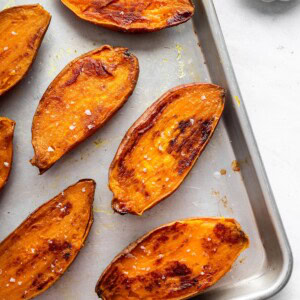 Seven roasted sweet potato halves on a baking sheet topped with flaky sea salt.