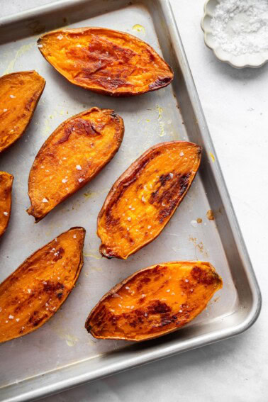 Seven roasted sweet potato halves on a baking sheet topped with flaky sea salt.