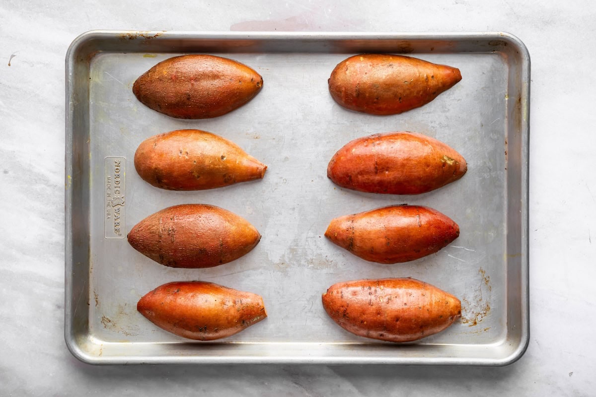 8 sweet potato halves on a baking sheet flesh side down ready to be roasted.