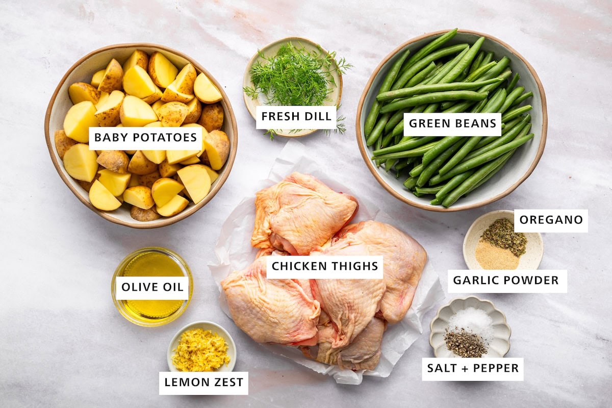 Ingredients measured out for sheet pan chicken and potatoes: chicken thighs, green beans, baby potatoes, fresh dill, olive oil, lemon zest, salt, pepper, garlic powder, and oregano.