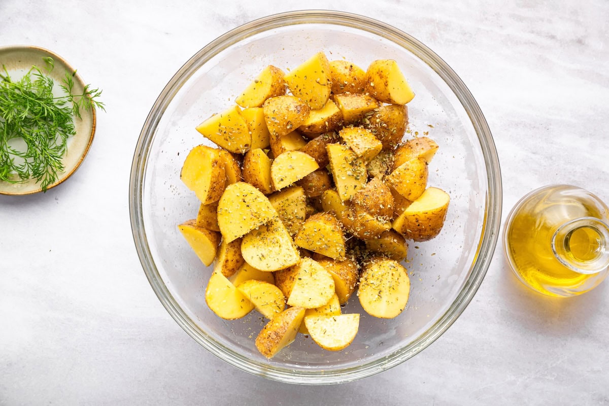 Diced potatoes in a glass bowl with dried herbs.