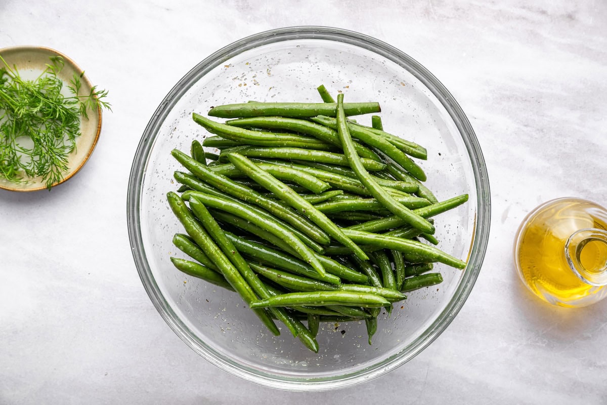 Seasoned green beans in a large glass bowl.