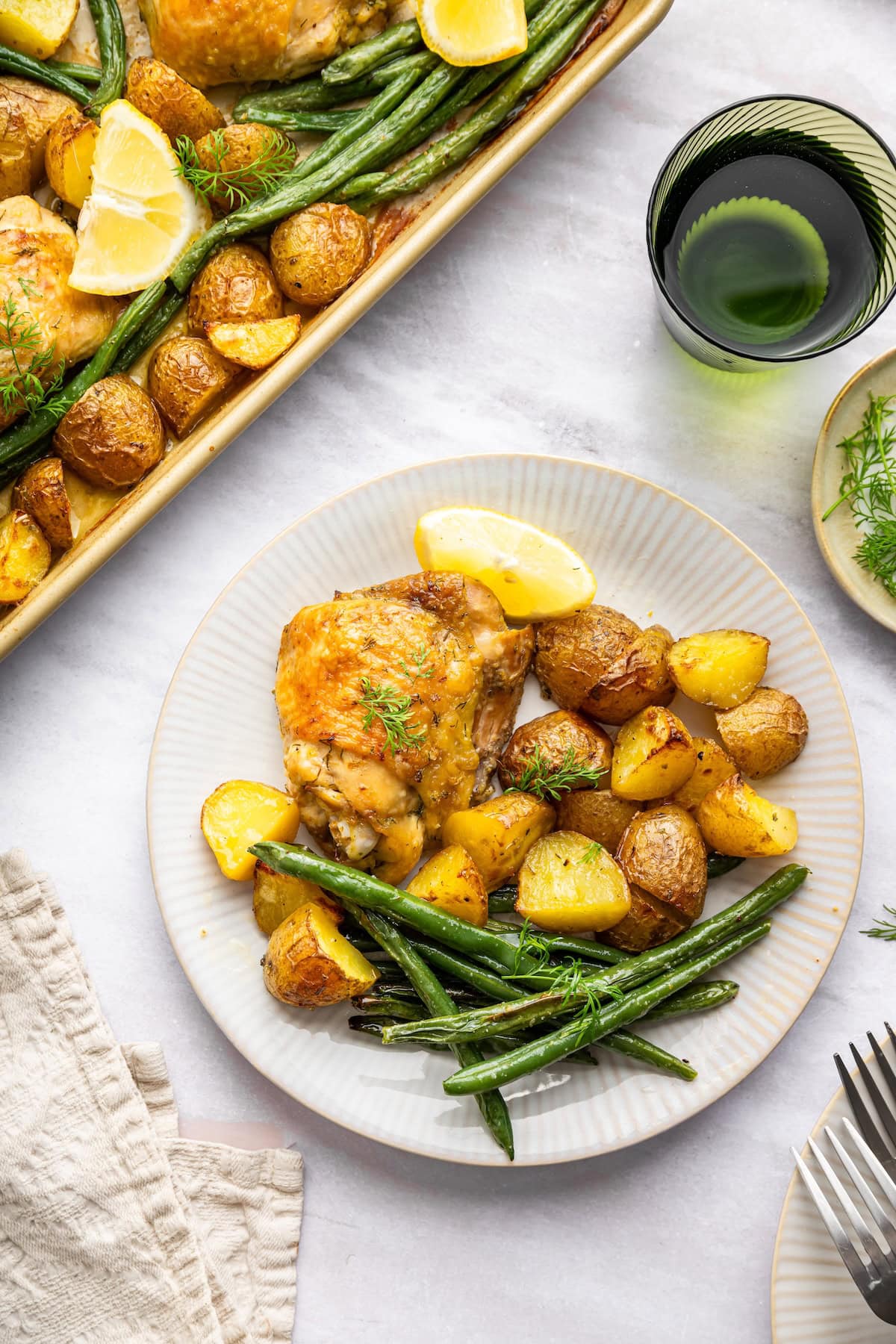 A serving of sheet pan chicken and potatoes with fresh dill and green beans on a plate.