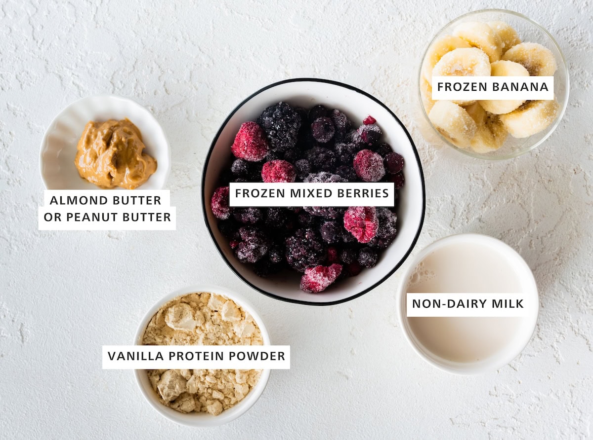 Ingredients measured out to make a Smoothie Bowl: vanilla protein powder, almond or peanut butter, frozen mixed berries, non-dairy milk and frozen banana.