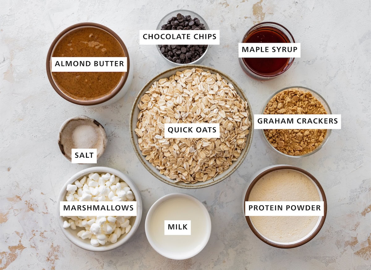 Ingredients for s'mores protein balls: almond butter, chocolate chips, maple syrup, graham crackers, quick oats, protein powder, milk, mini marshmallows and salt.