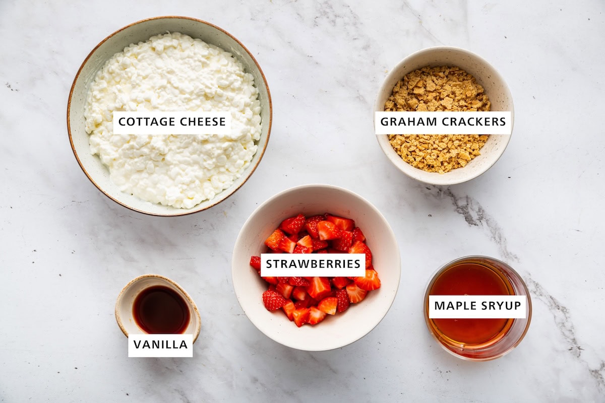 Ingredients measured out for strawberry cottage cheese ice cream: strawberries, cottage cheese, graham crackers, vanilla, and maple syrup.
