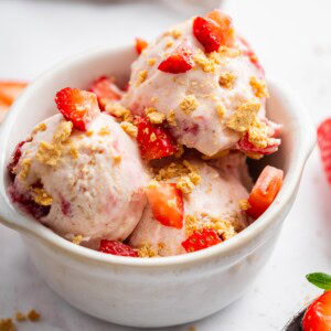 Scoops of strawberry cheesecake cottage cheese ice cream served in a bowl and topped with fresh strawberries and graham crackers.