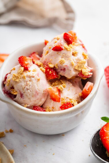 Scoops of strawberry cheesecake cottage cheese ice cream served in a bowl and topped with fresh strawberries and graham crackers.