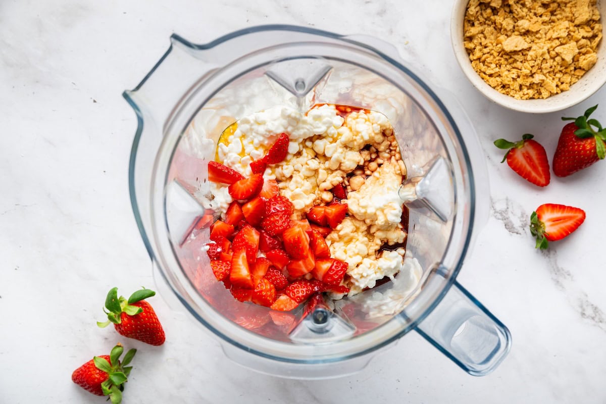 A blender with cottage cheese, fresh strawberries, maple syrup, and vanilla.