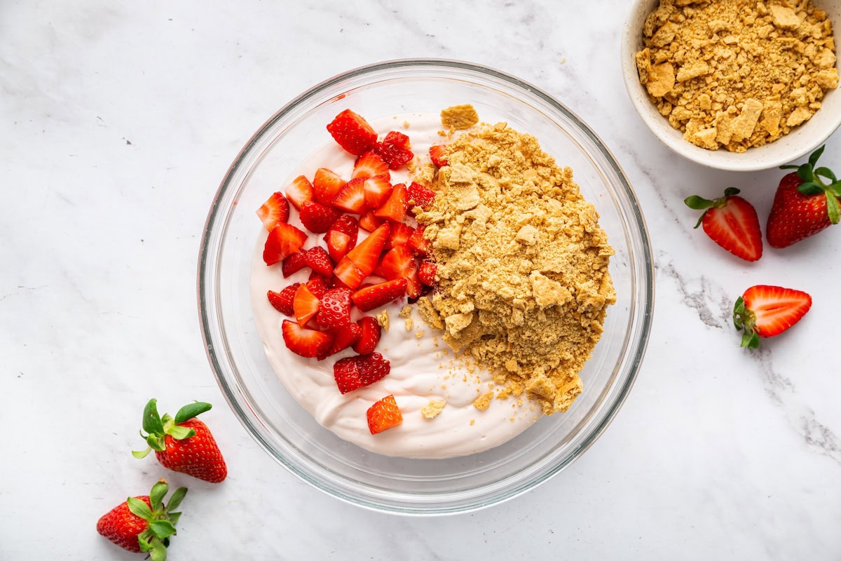 Fresh strawberries, crushed graham crackers, and an ice cream mixture in a large glass bowl.