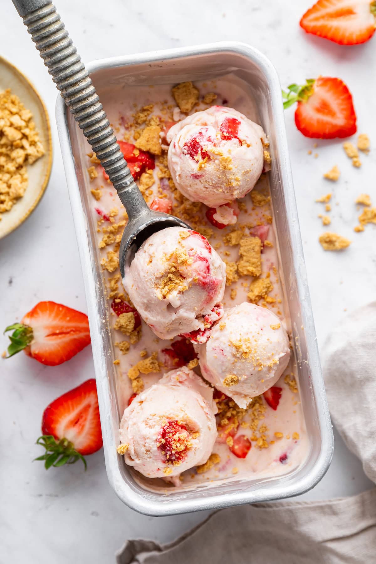 Strawberry cheesecake cottage cheese ice cream in a container and being scooped out with an ice cream scoop.
