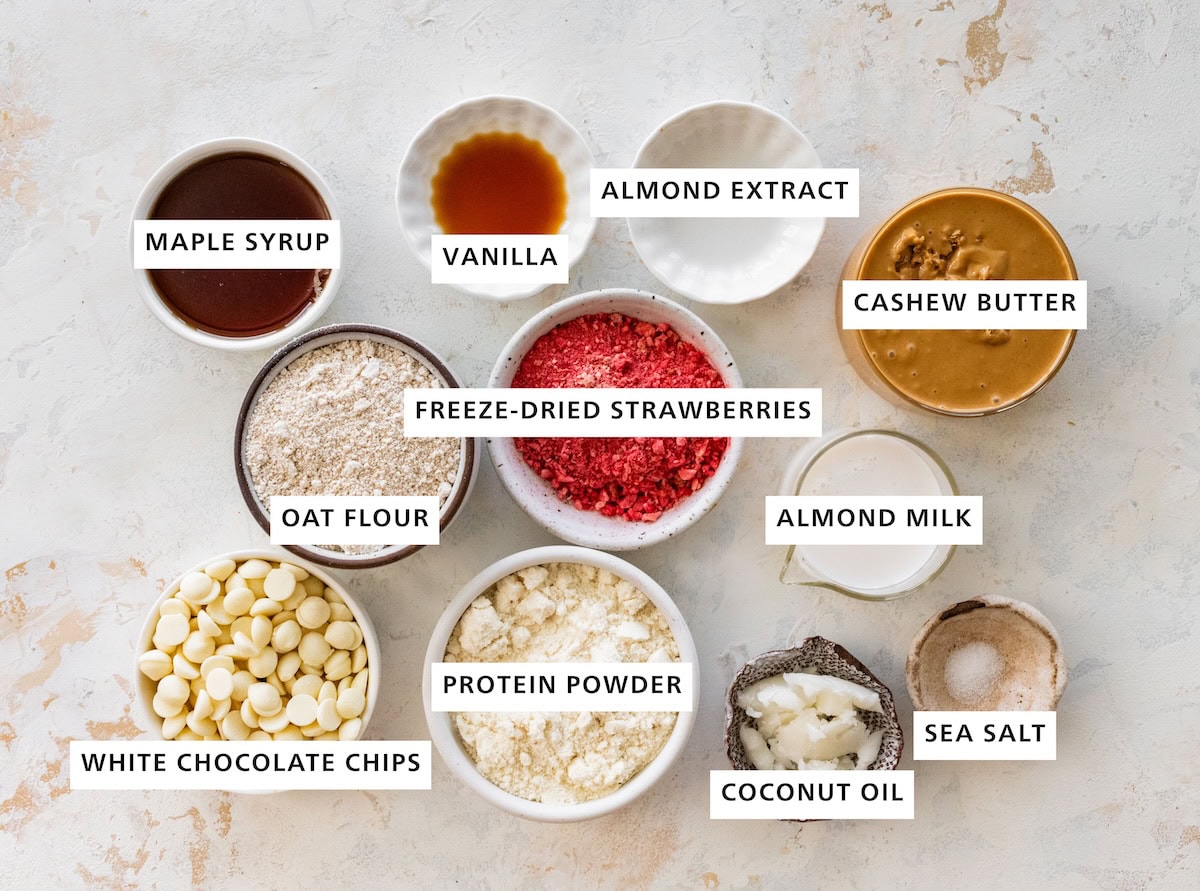 Ingredients for strawberry protein balls: maple syrup, oat flour, white chocolate chips, protein powder, coconut oil, sea salt, almond milk, cashew butter, almond extract and vanilla extract.