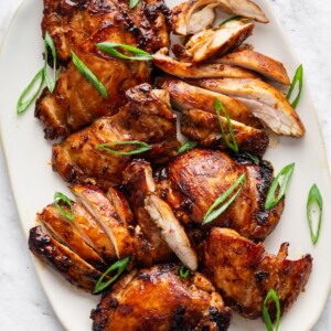 Teriyaki chicken thighs on a large plate topped with fresh green onion.