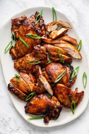 Teriyaki chicken thighs on a large plate topped with fresh green onion.