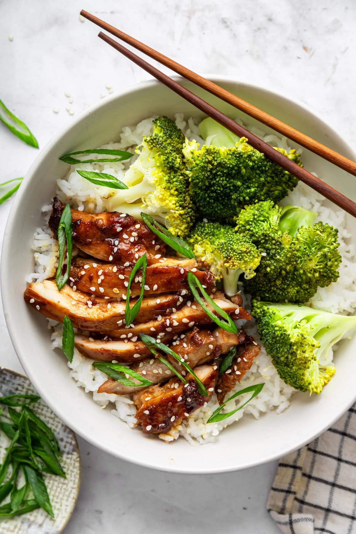Teriyaki chicken served in a bowl with white rice, broccoli, and a pair of chopsticks to the side.