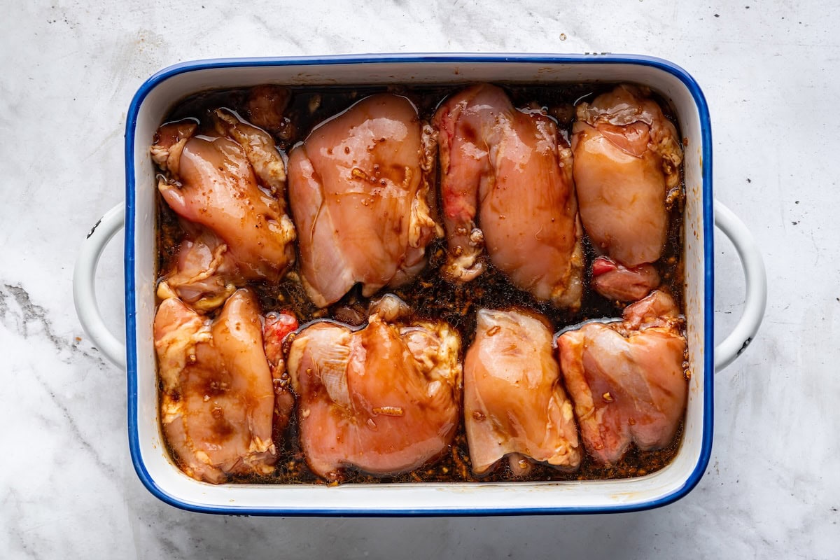Eight raw chicken thighs marinating in a large baking dish.