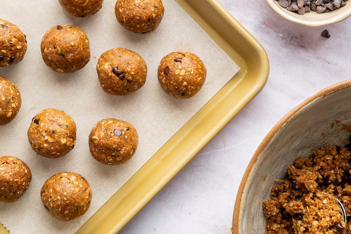 Zucchini bread protein balls rolled and spread out on a parchment lined baking sheet.