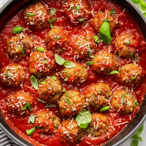 Zucchini meatballs in a skillet with marinara sauce, fresh basil, and parmesan cheese.